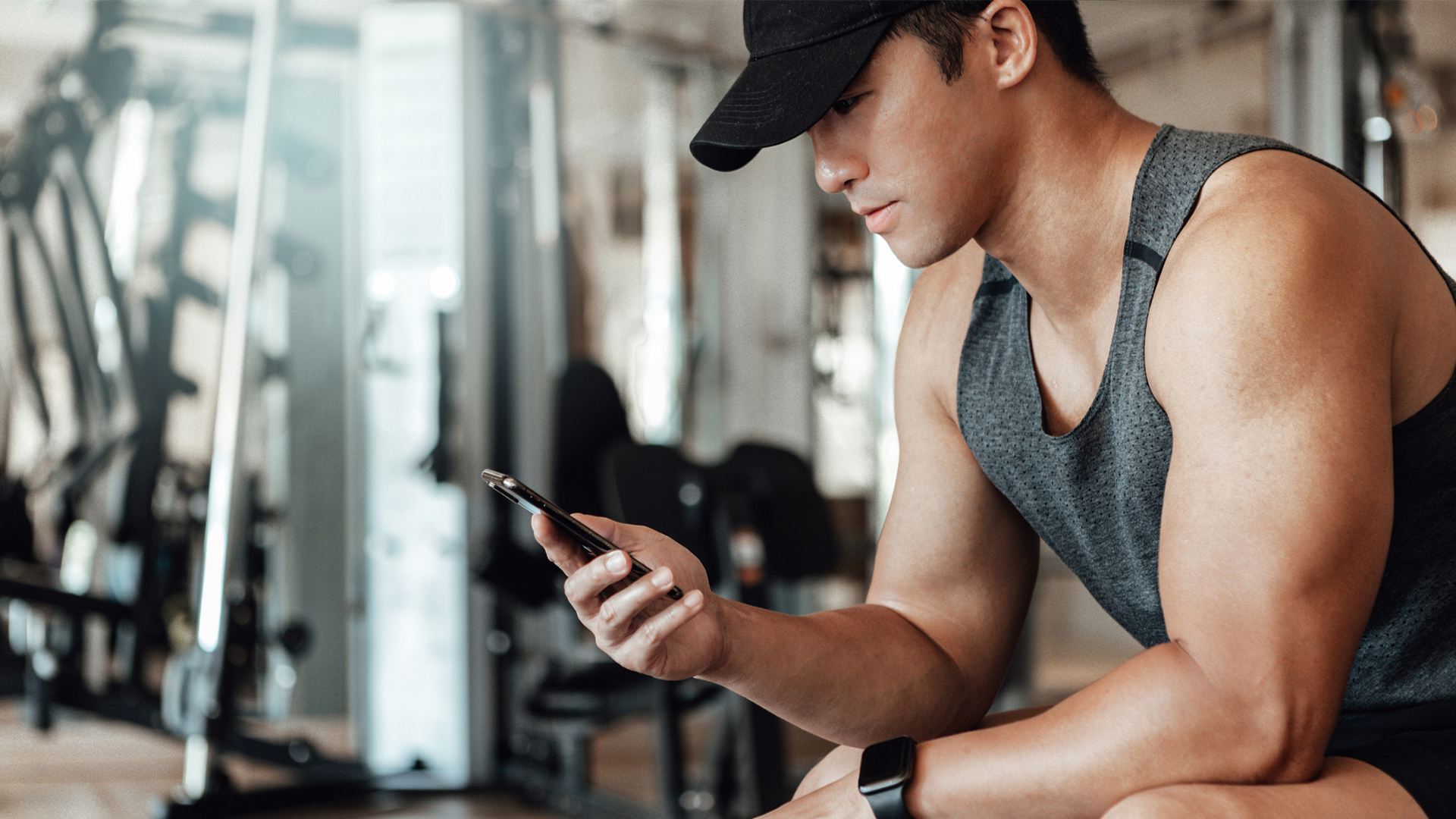 A man sits down at the gym as he looks at his phone