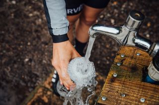 Cyclist holding a water bottle below a tap of running water