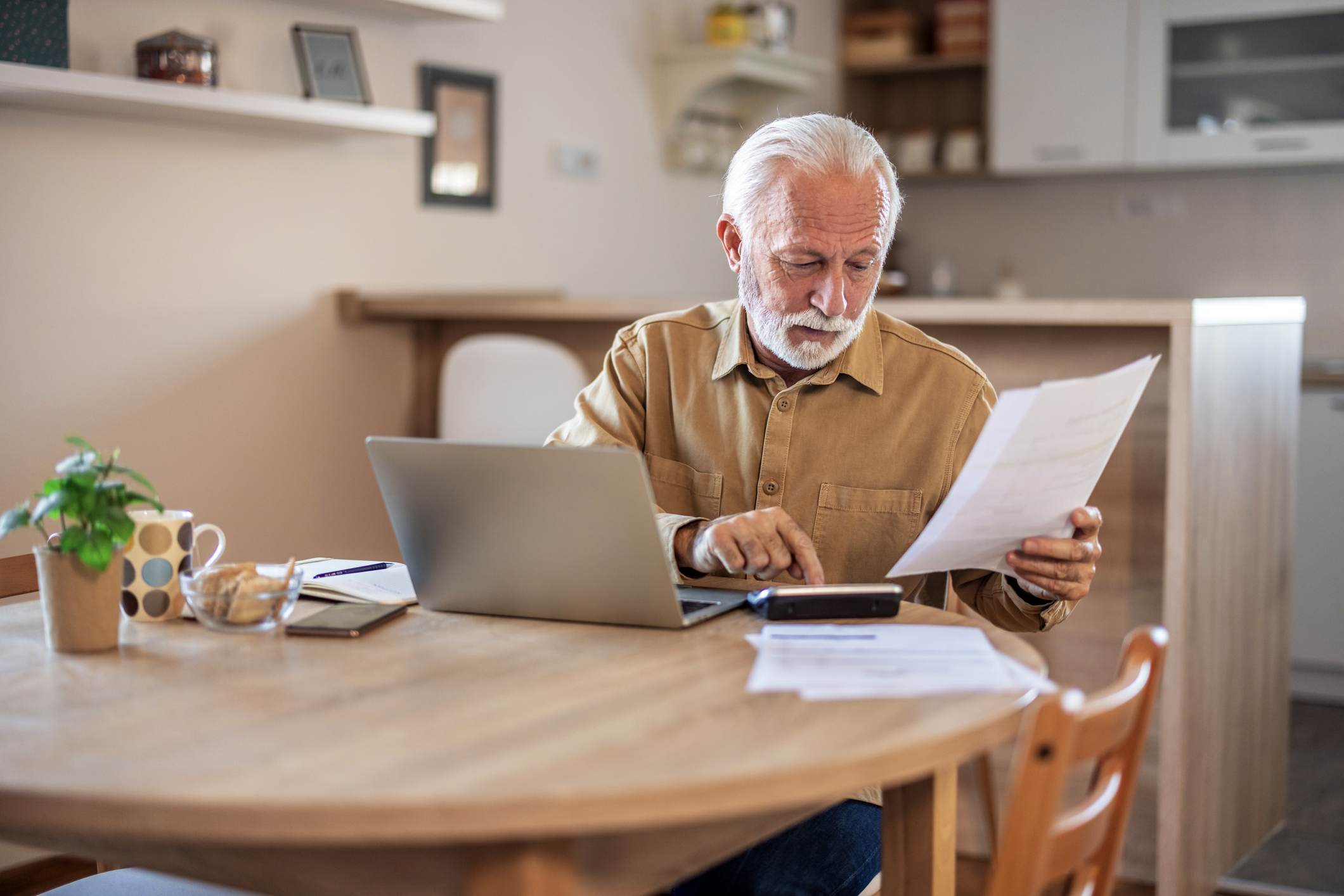 Man on laptop in a kitchen, reading pension and savings plan in his home