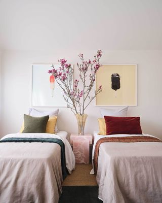 twin bedroom with colorful sheets, artwork of ice creams, a pink stone side table with a vase filled with cherry blossom branches