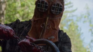 Ry Barrett holding a heavy chain with bloody hands while wearing a firefighter's mask in In A Violent Nature.