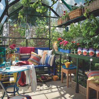 Seating area and potting bench with plants inside greenhouse in garden