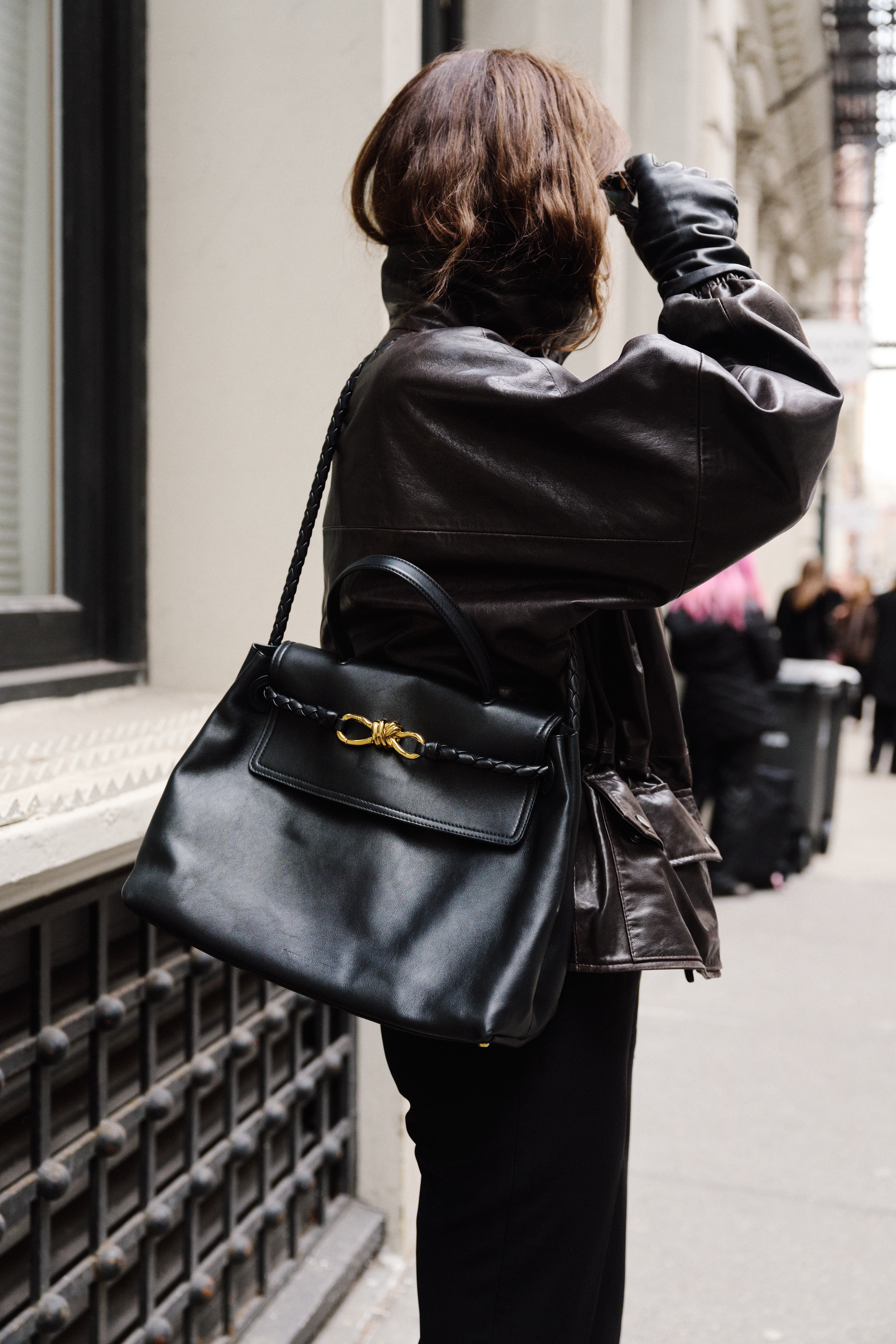 Eliza Huber wearing a brown leather jacket, black trousers, white loafers, and black sunglasses while carrying a black Bottega Veneta Ciao Ciao bag outside of the Kallmeyer show in Tribeca.