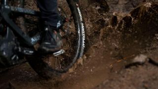 A close up of a rear wheel as a rider rides through a muddy puddle