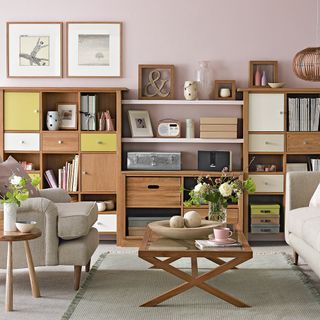A pale pink living room with wall of wooden storage