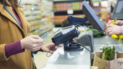 woman paying bill with credit card while standing by counter at supermarket