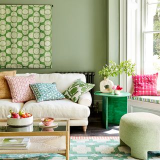 Green living room with decorative rug and textile artwork above cream sofa