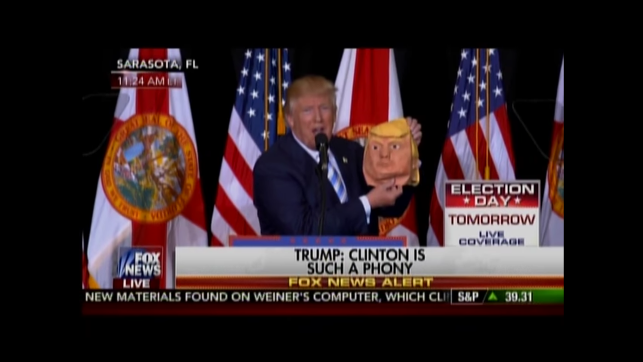 Donald Trump holds up a mask of himself.