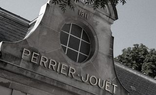 Black and white image Perrier-Jouët house, Pierre Jouet name sign at the top of a stone arch with round window, slate roof, top of a leafy tree, clear sky