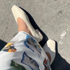 Woman wears white Sam Edelman ballet flats with white printed maxi skirt while standing on street and taking photo from above.