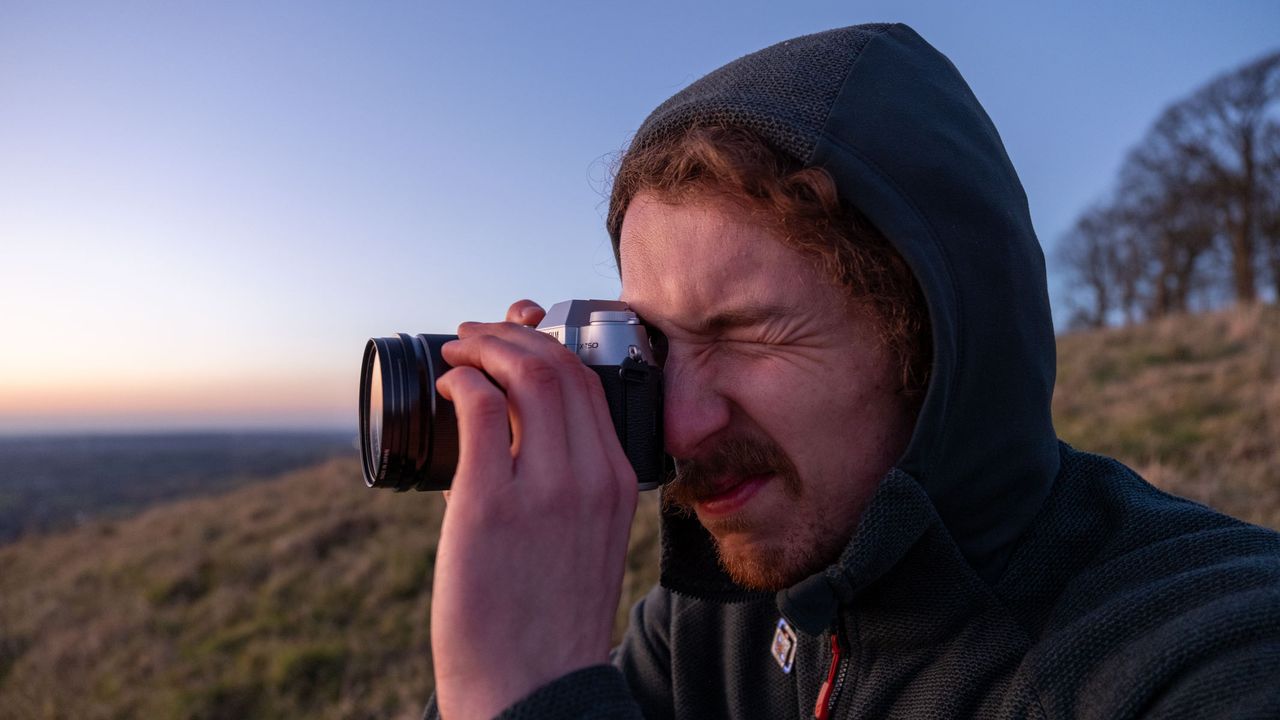 A man looking through a Fujifilm X-T50 with a field and sunset in the background.
