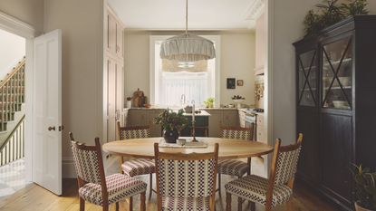 A cozy dining room with a round wooden table and five chairs. A low hanging fabric pendant above it. A blue hutch storage cabinet to the right.