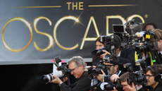 Photographers snap stars on the red carpet in front of a large backdrop that says 'The Oscars'