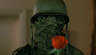 A man in an army mask holds a rose in 'The Prowler''