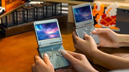 Anbernic RG SP handhelds being held by two people at desk.