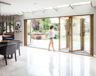 A woman opening a set of solid oak bifold doors in a large kitchen