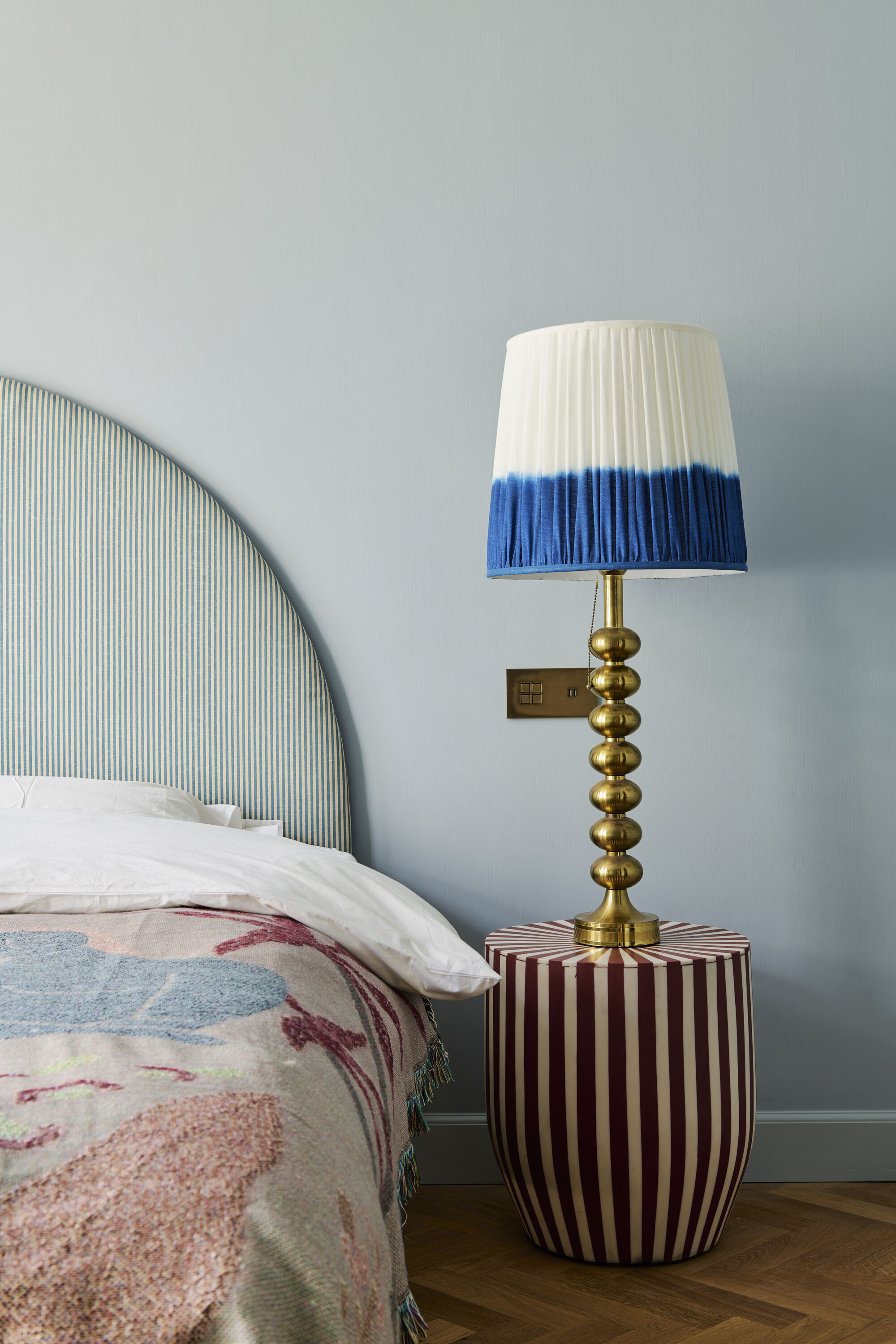 a blue and pink bedroom with a striped bedhead, patterned blanket, striped bedside table and blue and gold lamp