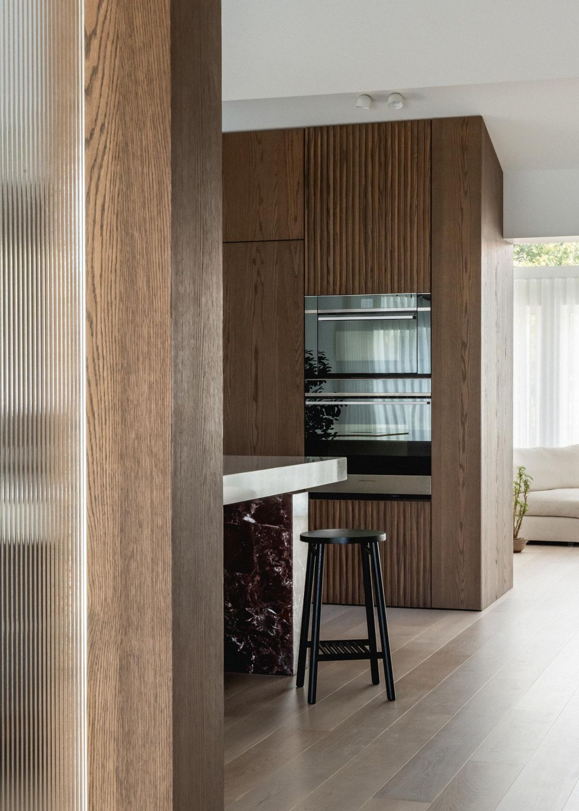 A convection oven above a conventional one in a kitchen with lots of wooden features as well as a kitchen island with a stool beside it.