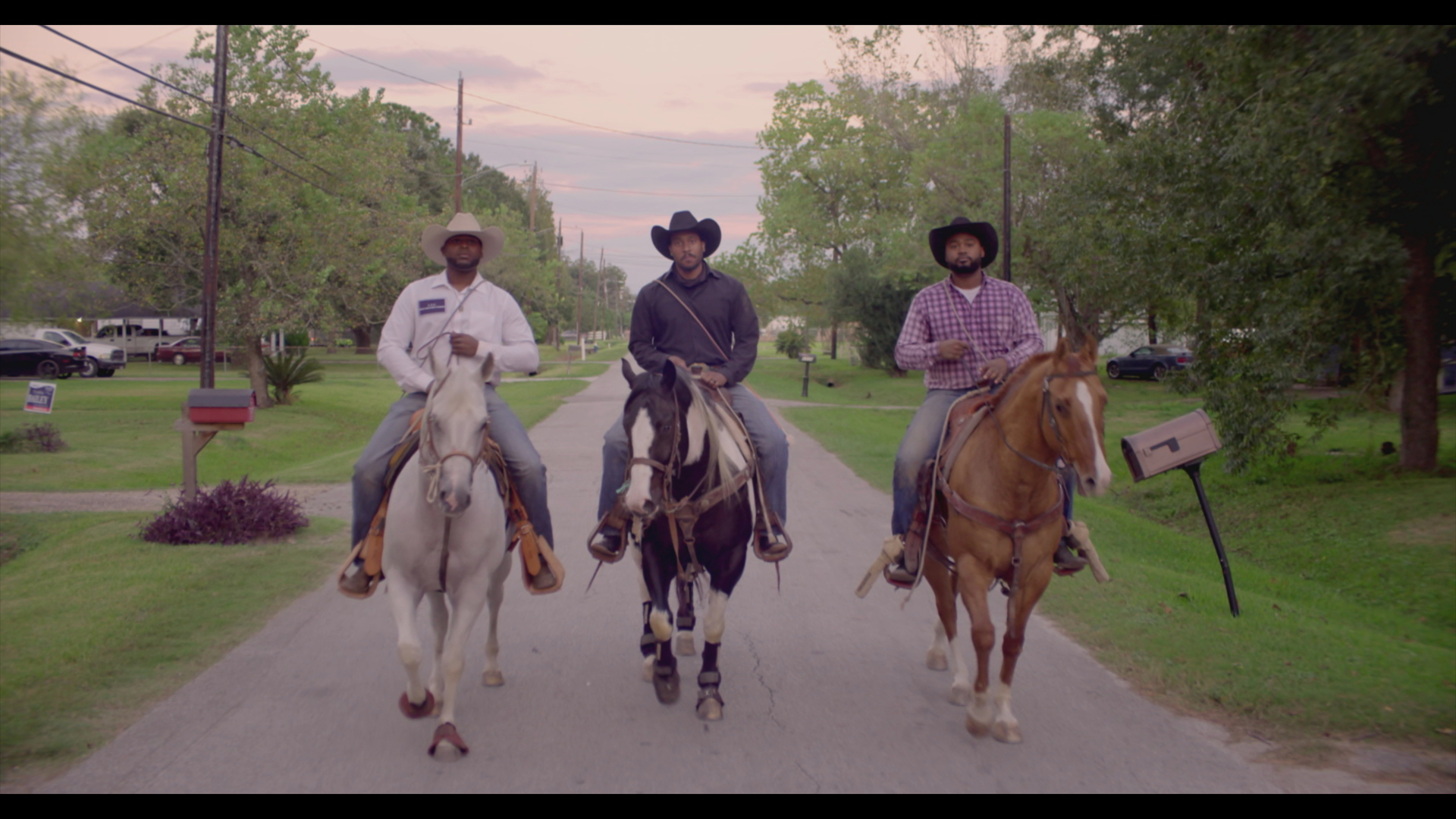 three male cowboys ride horses down a street in modern-day texas
