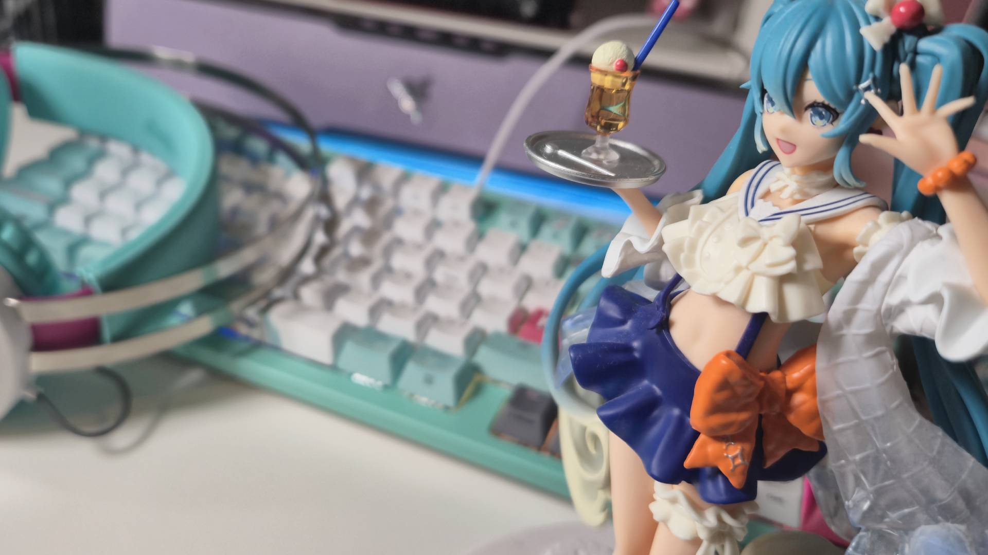 Photo by Rosalie Newcombe of the Asus TUF Gaming Hatsune Miku collection sitting on a desk in the background, with a FuRyu Miku figure in the foreground.