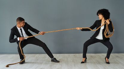 A man and a women in business suits fight in a tug of war battle.