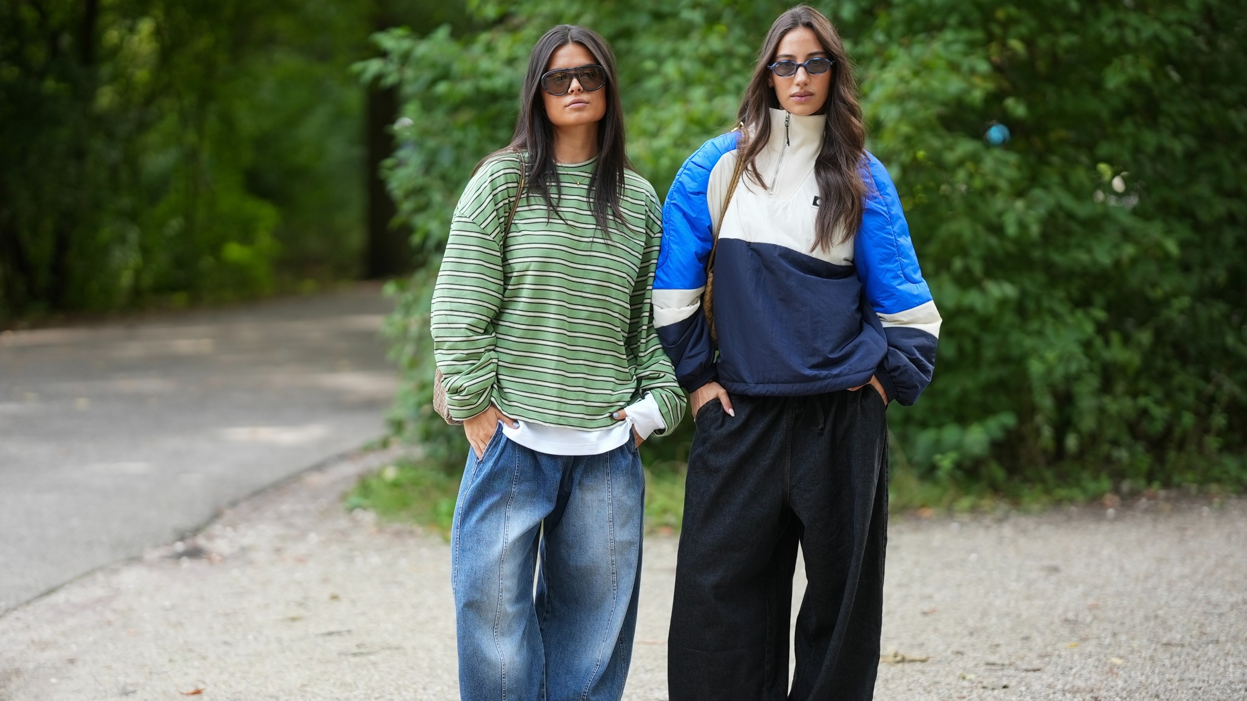 woman wearing a striped green oversized tshirt and jeans next to a woman wearing a funnel neck blue and white color blocked windbreaker with black trousers