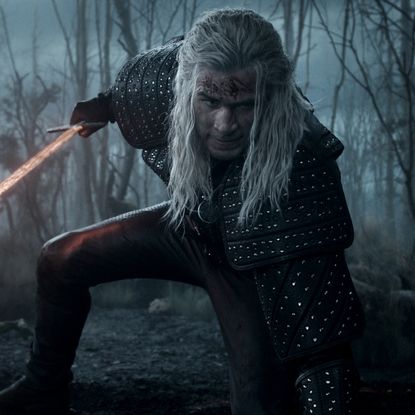 liam hemsworth as geralt of rivia wielding a red glowing sword while crouching down in the witcher season 4