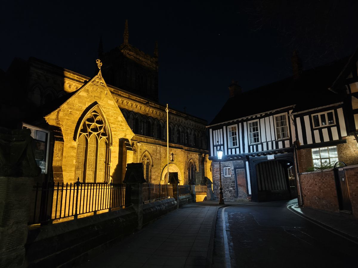 Old Tudor style building next to a church at night lit by a yellow light