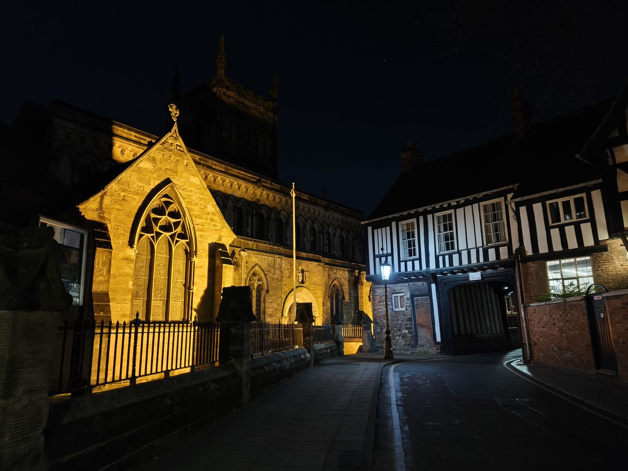 Old Tudor style building next to a church at night lit by a yellow light