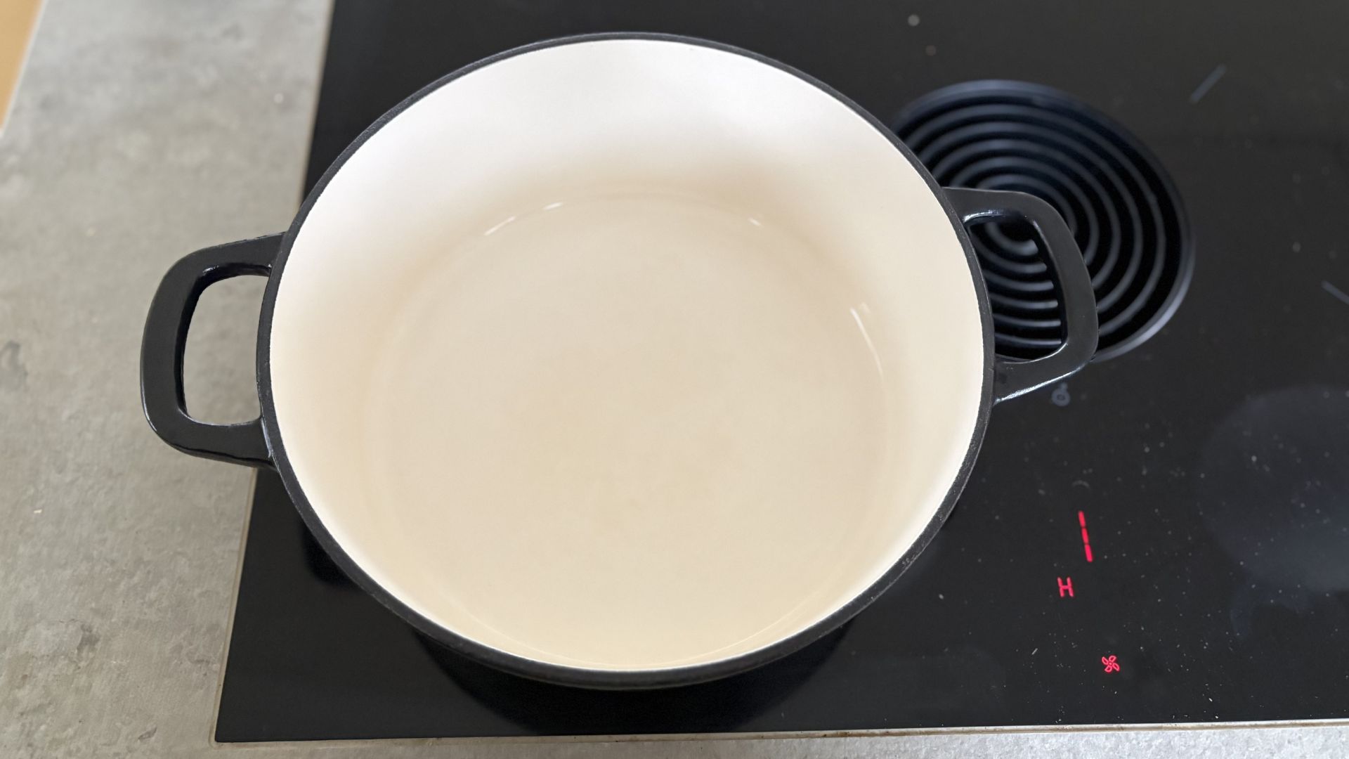 A stage of cleaning a burnt cast iron casserole dish on a hob