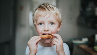 young blonde boy eating a peanut butter bagel
