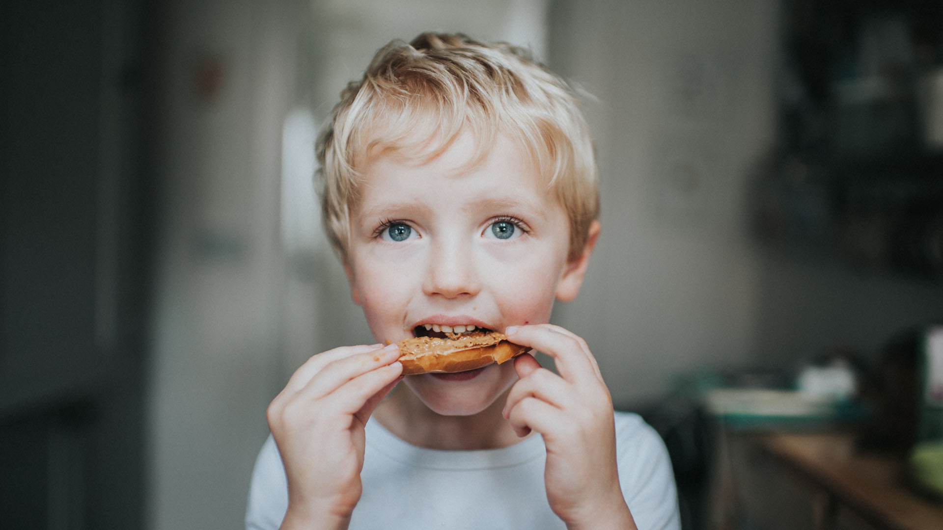 little blond boy eating a peanut butter bagel