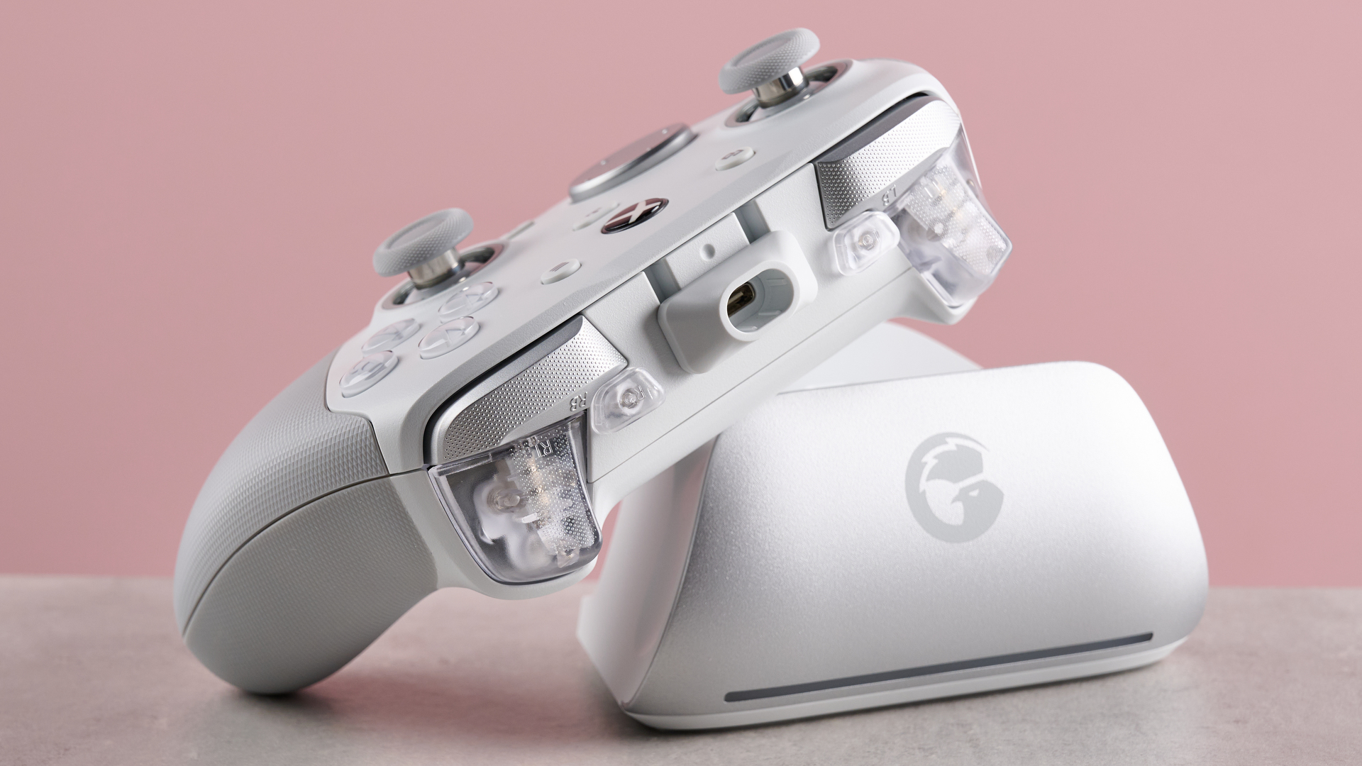 View of shoulder buttons of GameSir G7 Pro, leaning on its charging dock on desk with pink background