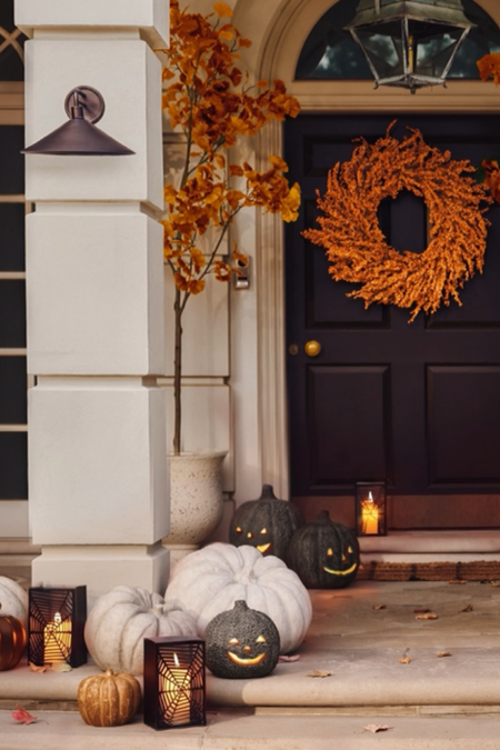 Festive Halloween porch featuring clusters of stone pumpkins, jack-o'-lanterns, pillar candles, and fall foliage flanking the front door. 