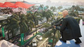 Agent 47 crouching with a sinper rifle on a roof overlooking the Miami race track in Hitman 2