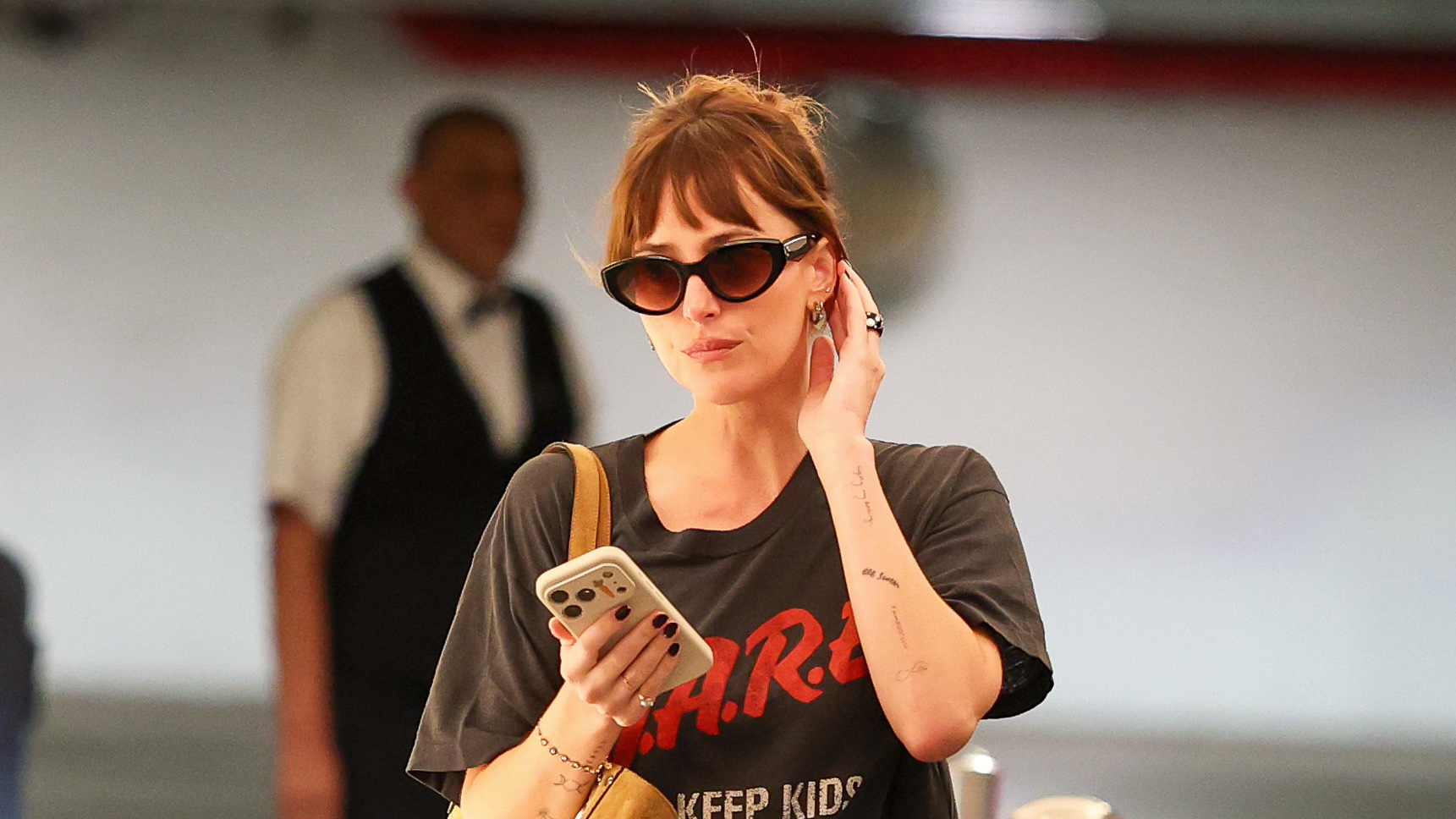 Dakota Johnson wearing a vintage D.A.R.E. T-shirt with silky black puddle pants and high-vamp ballet flats, carrying a Valentino suede tote