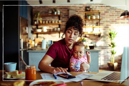 Young mother sitting at table looking at laptop while holding a baby on her lap
