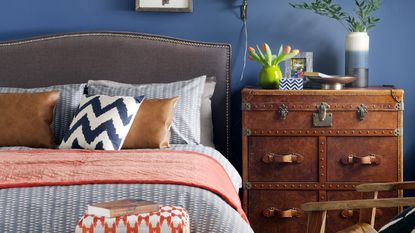 Blue bedroom with upholstered headboard, gallery wall and patterned footstool