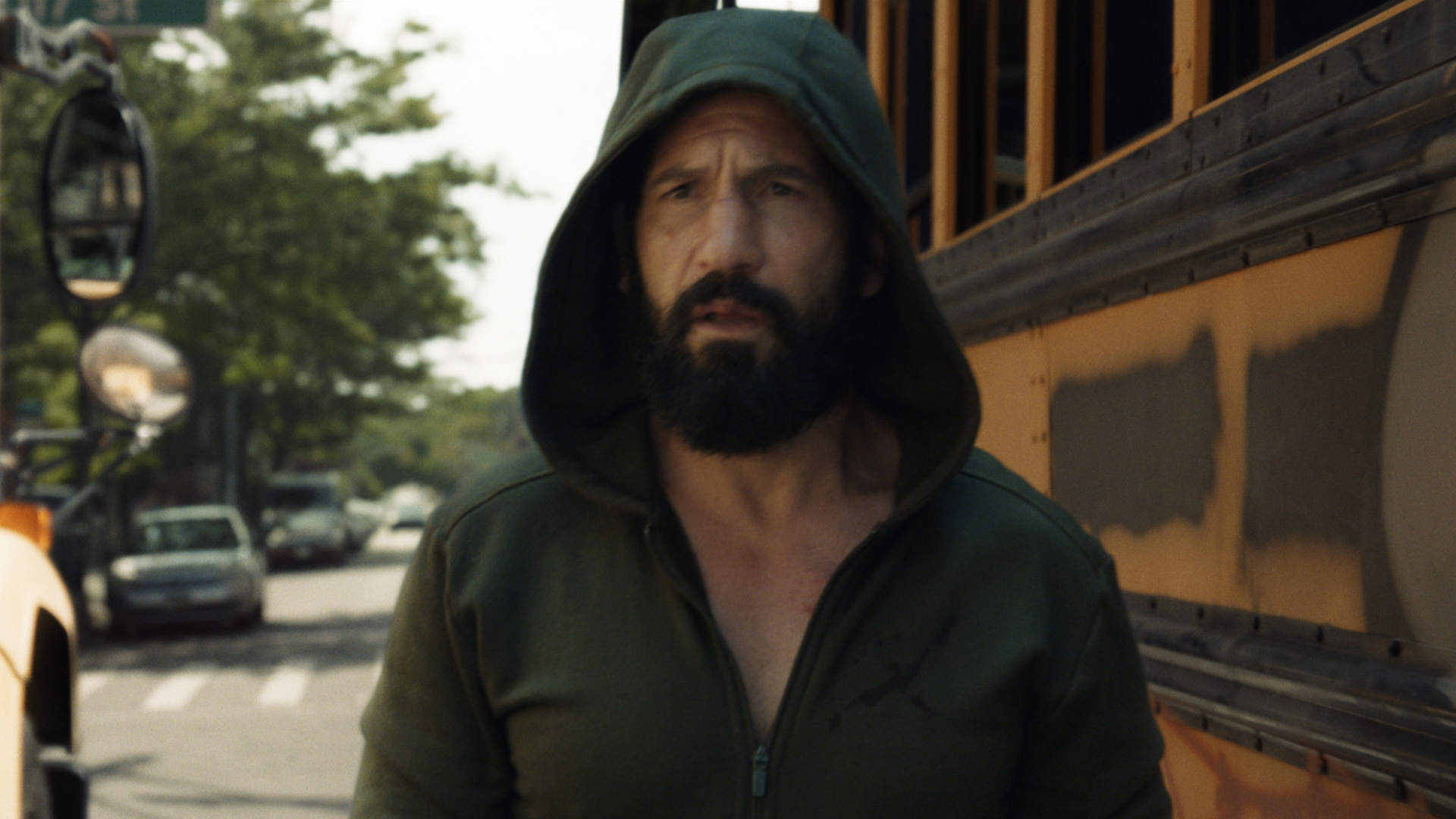 A hooded Frank Castle standing in front of a US school bus in The Punisher: One Last Kill