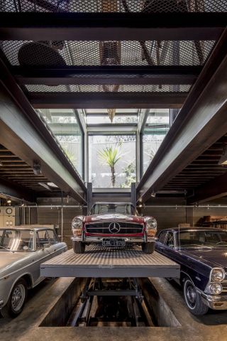 Inside an exhibition space with a front-on view of three old cars, focussing on a old sporty red Mercedes-Benz that has been elevated to a higher level.
