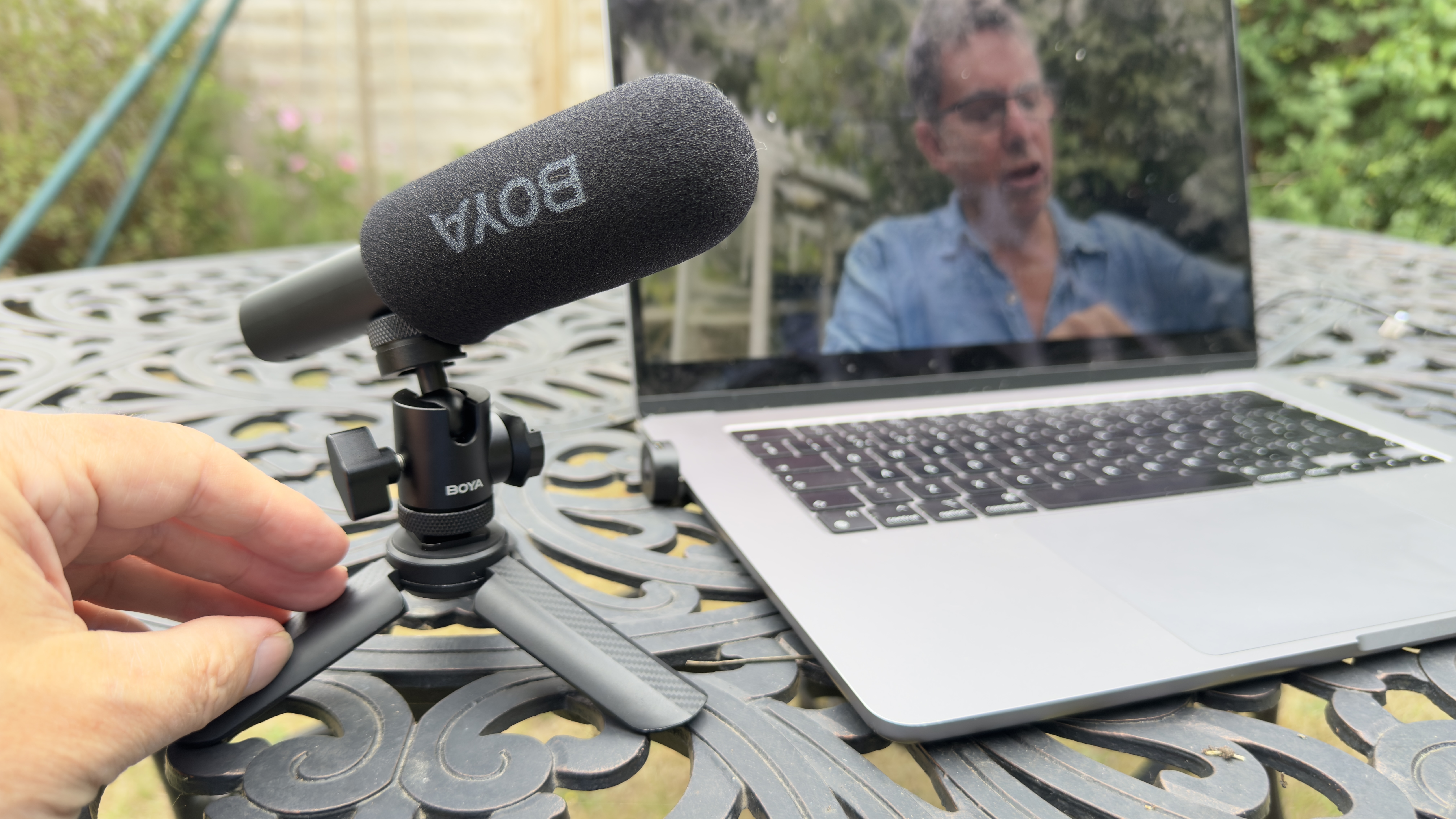 Shot of the Boya Magic’s gun mic configuration on a mini tripod sitting on a desktop adjacent to a laptop.