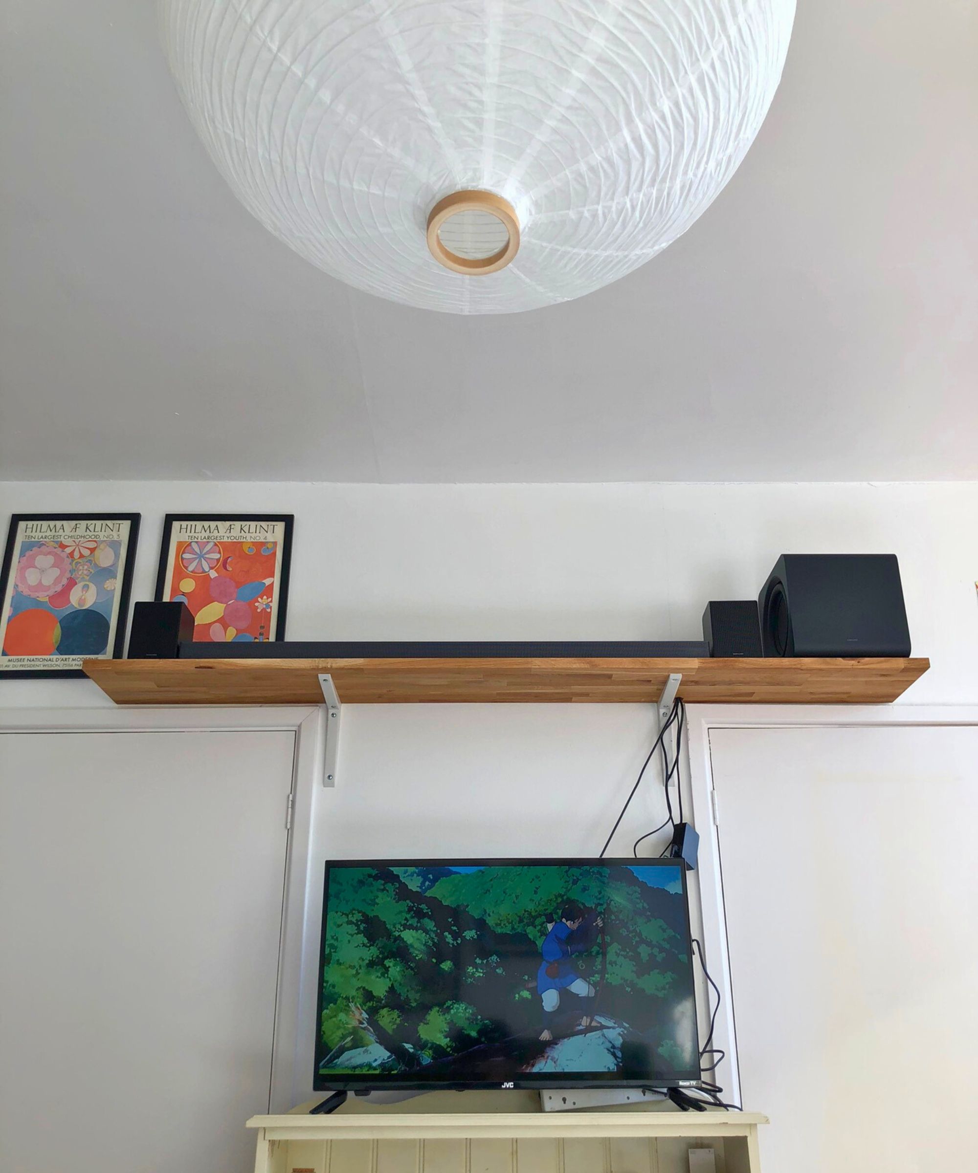 Samsung HW-QS750F soundbar on wooden shelf in Dan Fauzi&#039;s home, above TV showing Princess Mononoke and with two art prints pictured to the left.