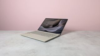 Three-quarter view of Asus Zenbook A14 open on a desk with pink wall in background