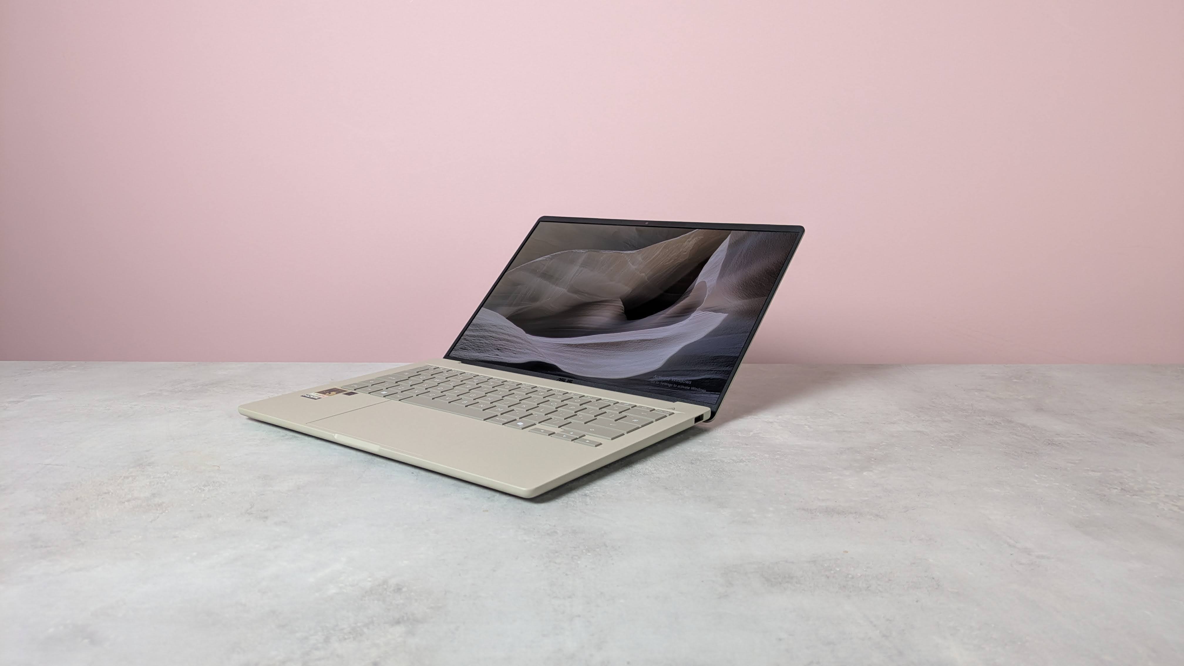 Three-quarter view of Asus Zenbook A14 open on a desk with pink wall in background