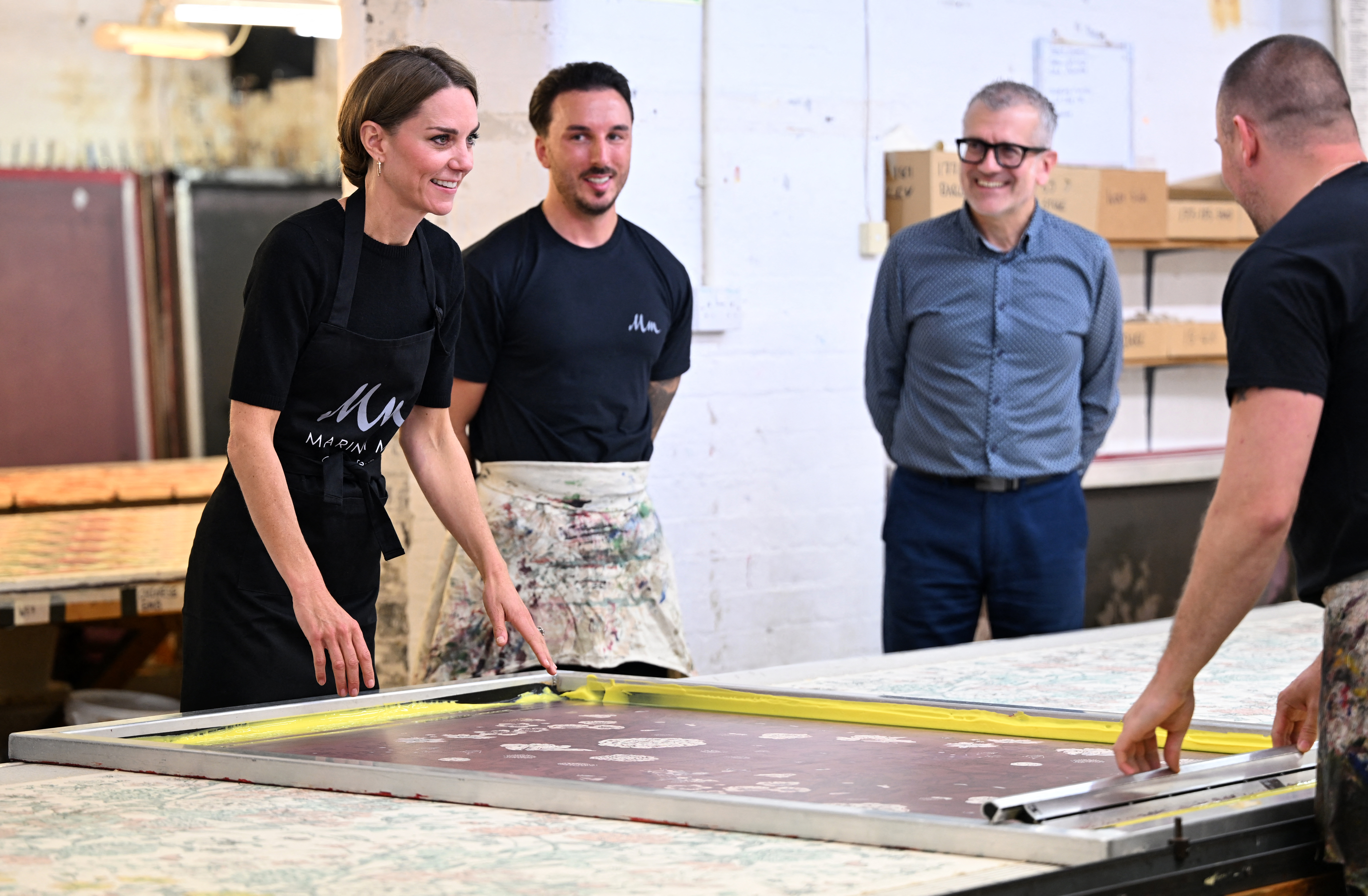 Kate Middleton standing in front of a screen printing plate wearing a black apron