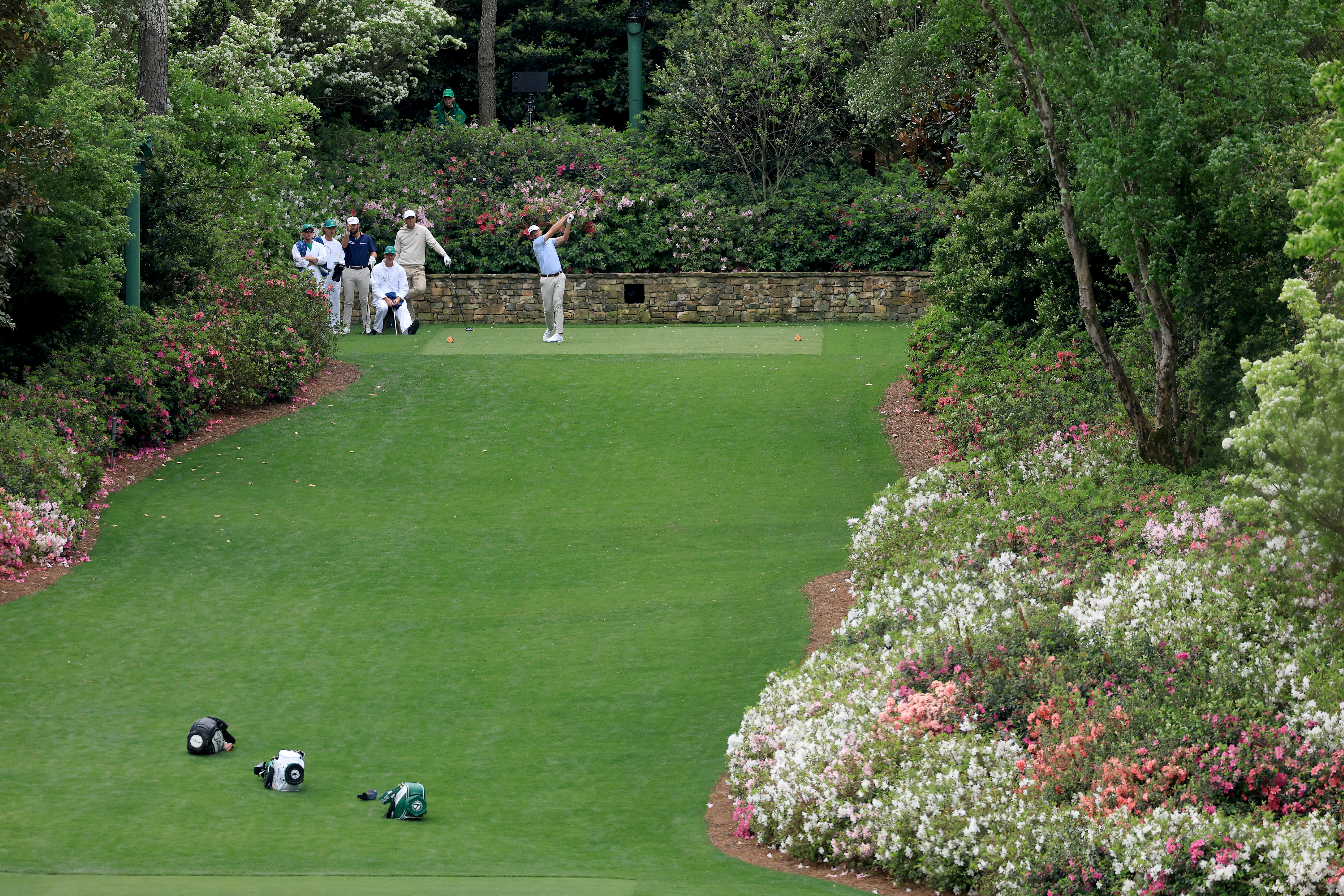 Sam Burns plays his tee shot on the 13th hole watched by Scottie Scheffler and Cameron Young during his practice round prior to the 2026 Masters Tournament at Augusta National Golf Club