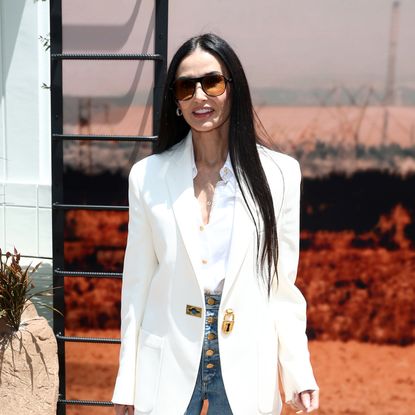 Woman with long straight hair wearing sunglasses, a white blazer and a white button up shirt.