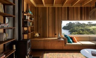 The living area at the retreat, with a perfect nook for reading. The couch is set against the wall which has a large panoramic window through which we see the ocean and natural landscape. The shelves on the walls are full of books.
