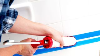 Person siliconing edge of bath/shower with caulk gun and using blue masking tape as a guideline