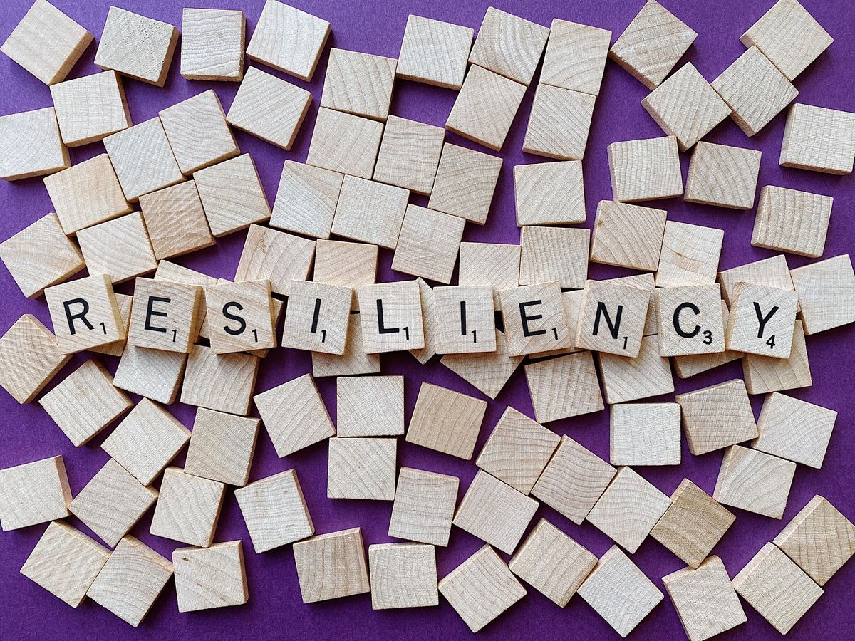 Square cubes with letters on them spell out the word &quot;resiliency.&quot; These cubes sit on top of blank square cubes against a purple backdrop.